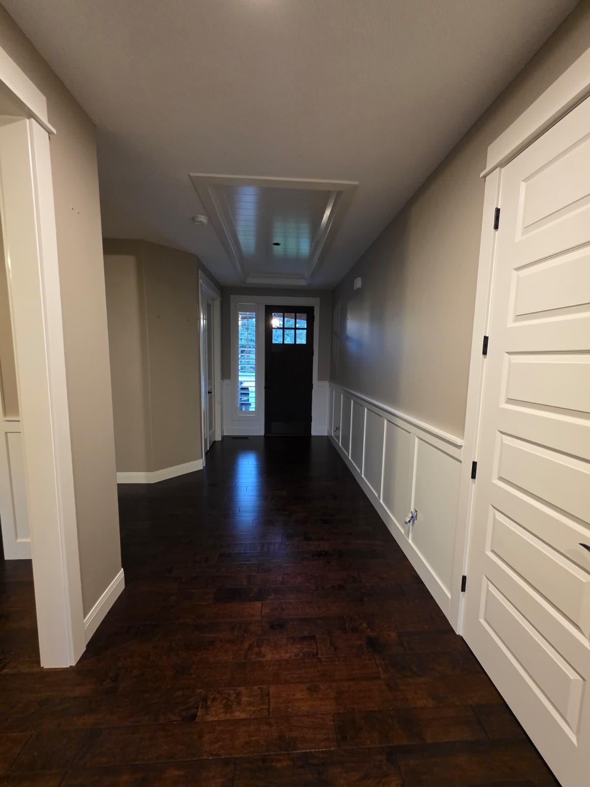 Finished hallway with taupe walls, white board-and-batten wainscoting, and dark hardwood floor