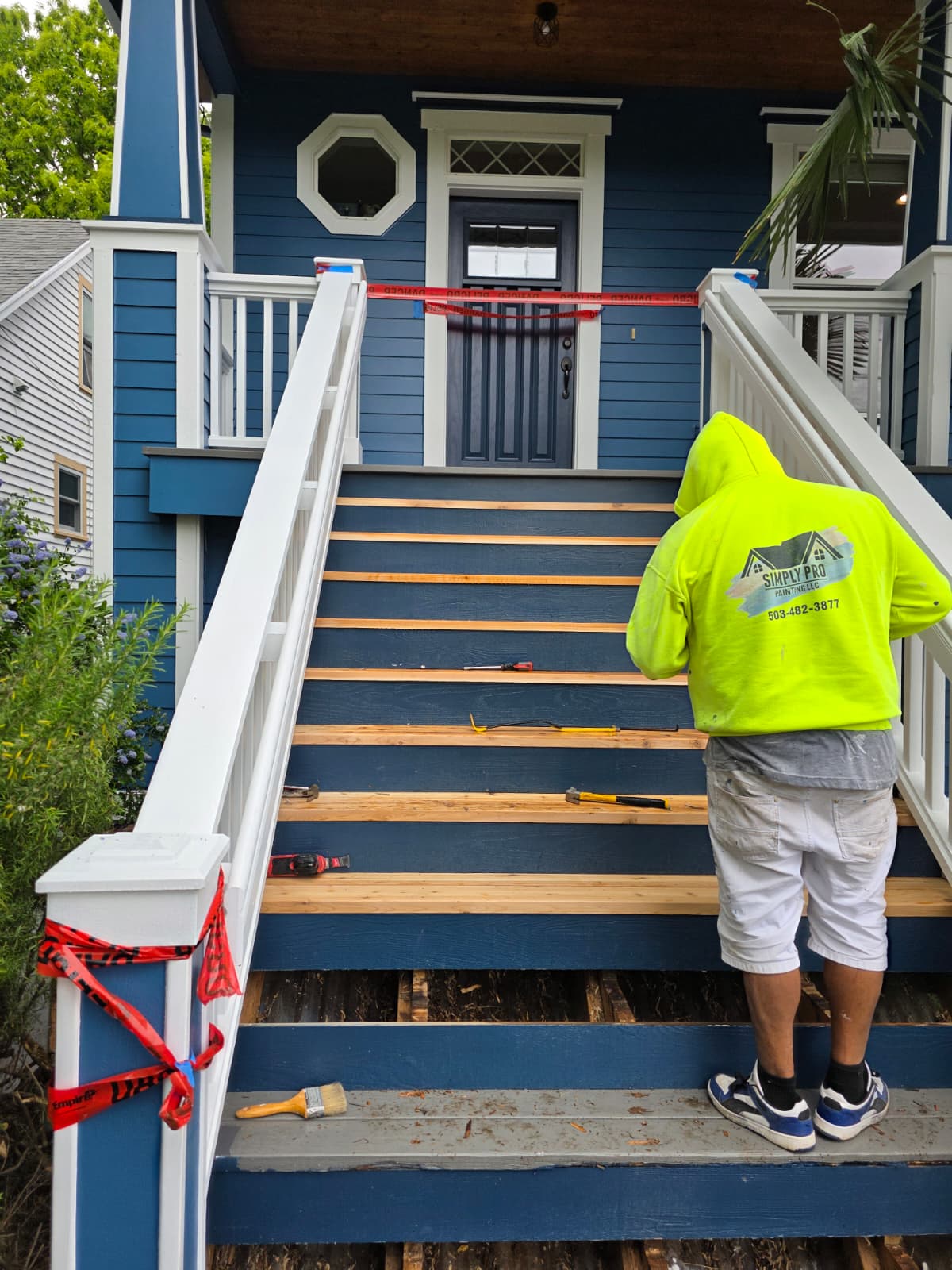 Simply Pro Painting crew member refinishing a front porch staircase on a navy blue home