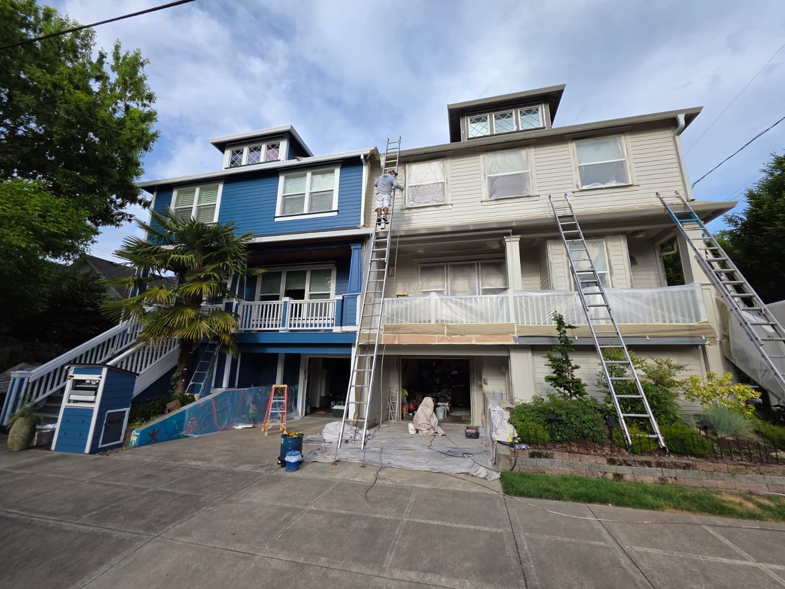 Exterior repaint in progress with one side of the home finished in blue and the adjacent side masked and prepped