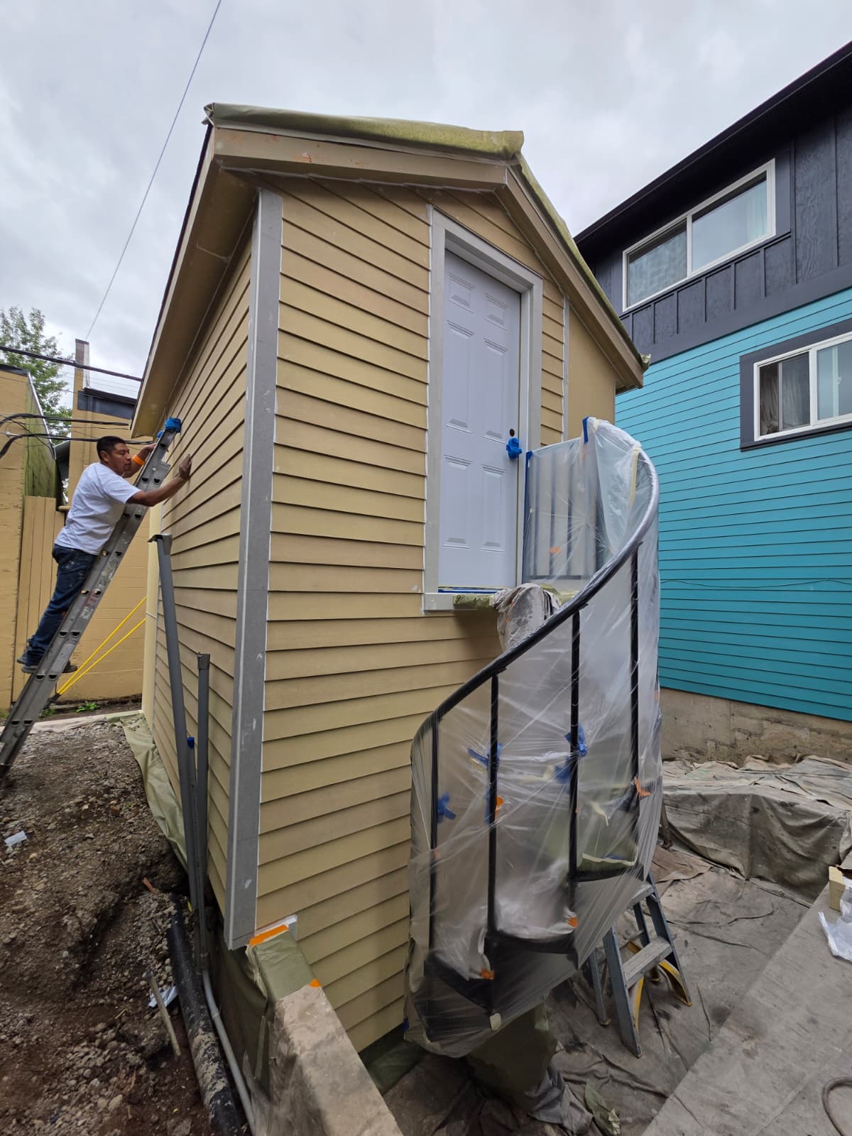 Simply Pro Painting crew member on a ladder prepping and painting exterior siding